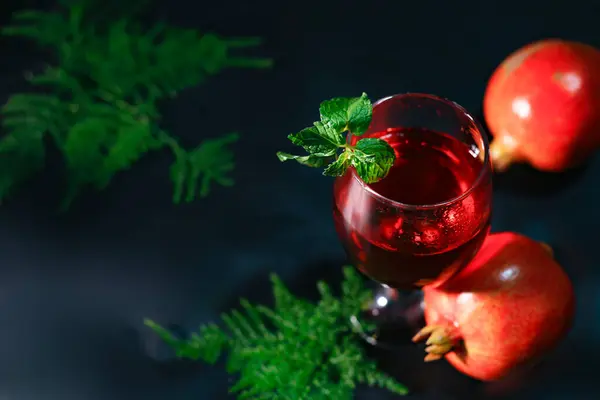 Olgun nar manzarası ve siyah arka planda bir bardak şarap ve bahsi geçen çiçeklerin devamı..