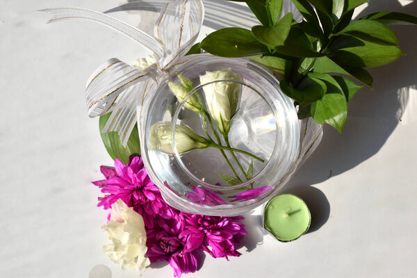 белые цветы в круглой вазе, украшенной бантом среди различных цветов и свечей на белом фоне