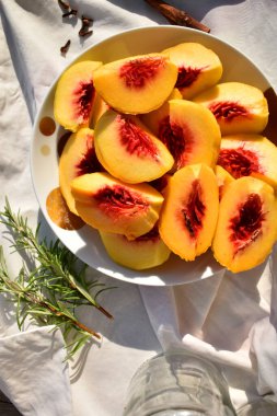Taze kesilmiş şeftali dilimleri, tabağa doldurulmuş, biberiye filizi ve karanfil, yakın çekim, üst manzara