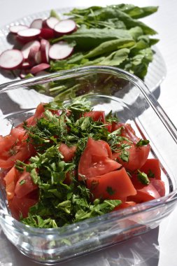 Kare cam tabakta kırmızı domates ve yeşilliklerden yapılmış salata ve turp dilimleri ve marul yapraklarıyla dolu bir tabak.