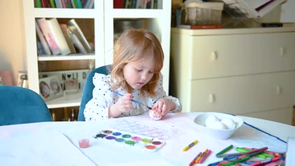 ダイナーのテーブルに座っている小さな女の子は イースターエッグを描き 図面を作り 創造的であること 彼女は卵の茶色を１つ描いている — ストック動画