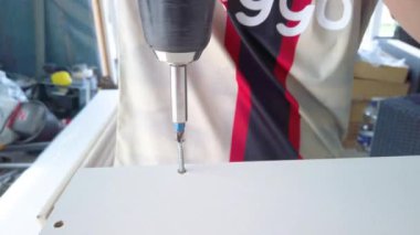 Genç çocuk babasının yeni mutfağı için dolapları toplamasına yardım ediyor. Çocuk vida takmak için vida makinesi kullanıyor. 4K