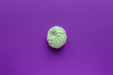 Renkli kremalar serpiştirilmiş rengarenk kremalı, mor bir arka planda. Çerçevenin ortasında tek bir yeşil pasta var. Etrafta bir sürü kopya alanı var.