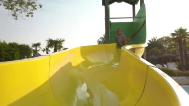İtalya 'daki Peschiera del Garda' daki Bella Italia kamp alanında küçük sarı bir su kaydırağından kayan tatlı bir kız. Sıcak ve güneşli bir yaz günü. Yavaş çekim 4K video