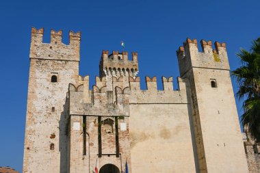 Castello Scaligero di Sirmione, Sirmione - İtalya 11 Eylül 2023. Sirmione, Garda Gölü, İtalya 'daki Scaligero de Sirmione kalesinin editör resmi. Güneşli bir yaz günü. Kalenin tepesinde İtalyan bayrağı sallanıyor..