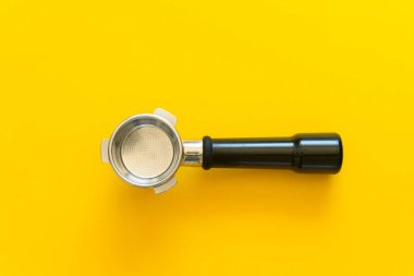 Sarı arka planda duran filtre sepetli boş espresso iskele filtresi. İskele filtresi, çerçevenin ortasında yatay olarak yatar.