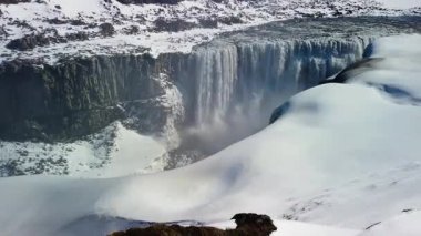 İzlanda 'daki ünlü Dettifoss şelalesinin stok videosu. Dettifoss İzlanda 'nın en büyük şelalesidir ve Avrupa' nın en güçlü şelalesidir. Şelalenin etrafındaki arazi karla kaplıdır. Güneşli bir bahar günü.