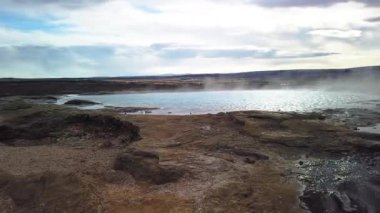 İzlanda 'nın en ünlü sıcak su gayzeri kaynıyor ve püskürmeyi bekliyor. Geysir 60 metreye kadar kaynar su fırlatabilir. Kamera sağa kayıyor.