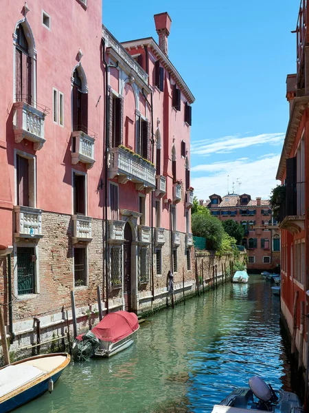 Picturesque old pink building on canal in Venice, Italy. Beautiful architecture surrounded by boats parked on the water on sunny spring day in Italian landmark.