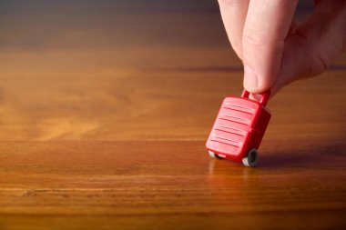 Male hand carrying miniature toy suitcase. Concept of travel, passenger with luggage. Travel insurance, booking and planning.