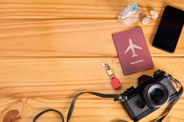 Top view of travel essential equipment on wooden table. Passport and padlock locked on miniature toy suitcase, camera and mobile phone. Travel insurance, safe travel and travel planning. Copy space.