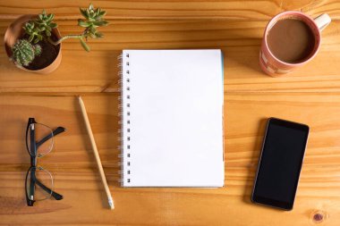 Top view of blank open notebook without lines on wooden table with pencil, eyeglasses, mobile phone, cup of coffee and succulent plant. Working table background mockup.