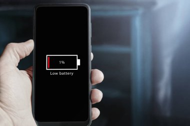 Close up of male hand holding smartphone with low battery icon on the screen indicating that battery level is at one percent. Battery drain on mobile phone.
