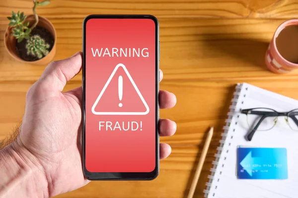 Man holding mobile phone with red screen and fraud text alert and icon. Scam concept, internet security. Protection against websites that can steal personal information.