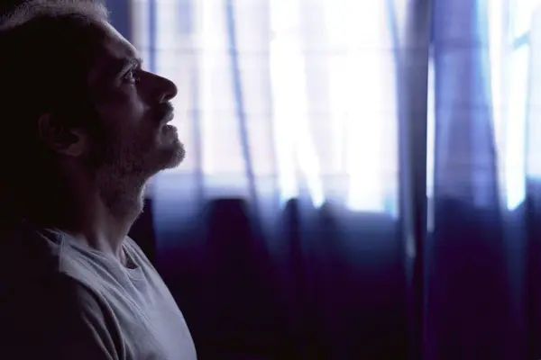 Karanlık odada ağlayan depresif genç sakallı adam. Pencereli loş ışık. Depresyon, akıl sağlığı, keder ve yalnızlık kavramı.