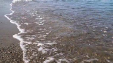 Temiz suyun altında dalgalarla dolu çakıl taşı plajı. Dalgalar çakıl taşlarında yüzer.