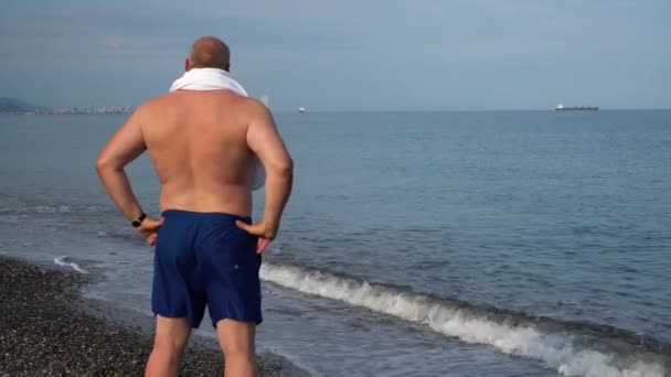 タオルを持った男が海を見る — ストック動画