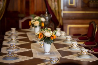 Masanın üzerinde çiçekli bir vazo ve çay için eski bir kap var..