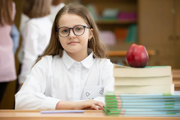 Schoolgirl in glasses at the desk. Girl in the classroom with books and an apple. Secondary school. Back to school.