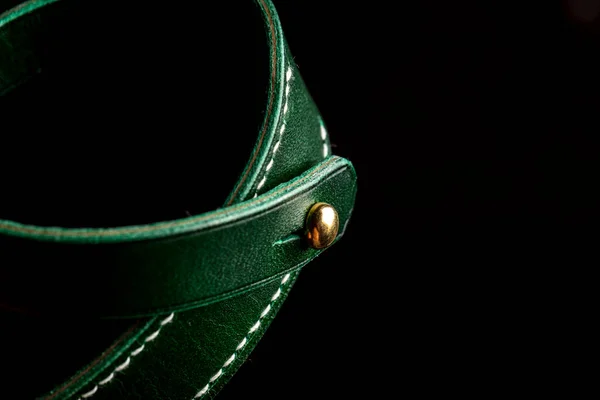 Part of a leather product or belt in green on a black background.