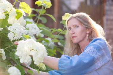 Beautiful elderly woman posing in the garden with a bouquet of flowers.
