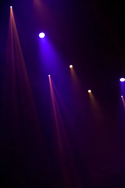 Purple beams of light from stage spotlights on a dark background.
