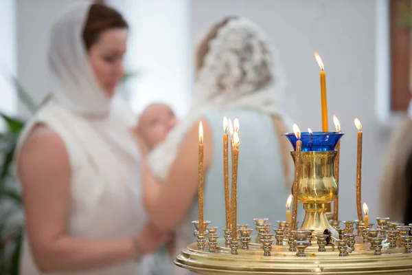 Blurred rite of Orthodox baptism against the background of burning candles.