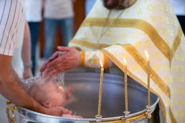 Blurred rite of Orthodox baptism against the background of burning candles.