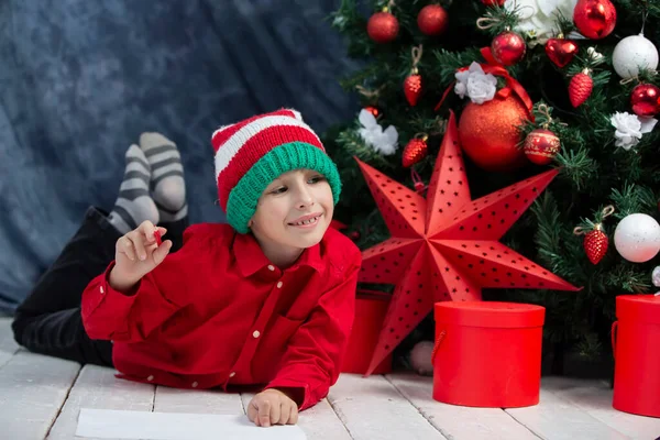 Little boy writes a letter to Santa Claus, thinks about gifts for Christmas.