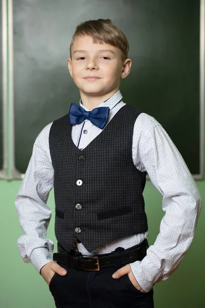 Portrait of a handsome schoolboy in elegant clothes at the blackboard. A smart and successful student, an excellent student.