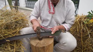 A man sharpens a scythe with a special hammer.