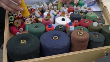 A woman's hand chooses a white spool for sewing clothes. Colorful spools of thread in a box. Self made. Women's hobby.