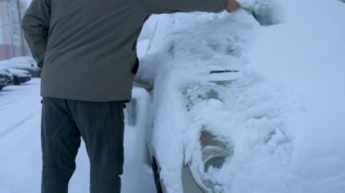 A man cleans his car after a snowfall on a frosty day. Cleaning and cleaning the car from snow on a winter day.