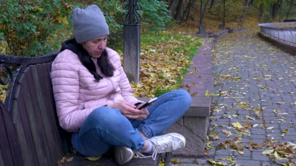 Warmly Dressed Woman Sits Bench Autumn Park Looks Mobile Phone — Stockvideo