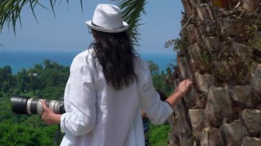 Photographer woman enjoying the ocean view near the palm tree on the mountain.