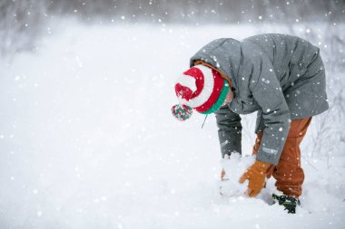 Bir çocuk karlı bir arazide kartopu yapıyor. Bir çocuk kışın karla oynar.