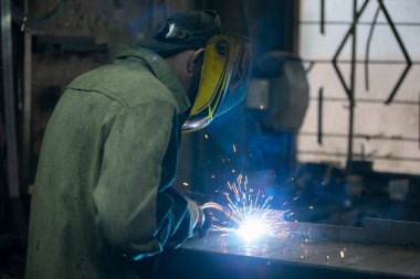 Bir kaynakçı bir fabrikada metalle çalışır..
