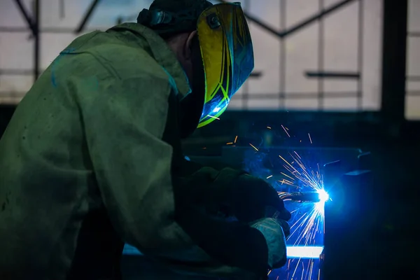 A welder works with metal in a factory shop.