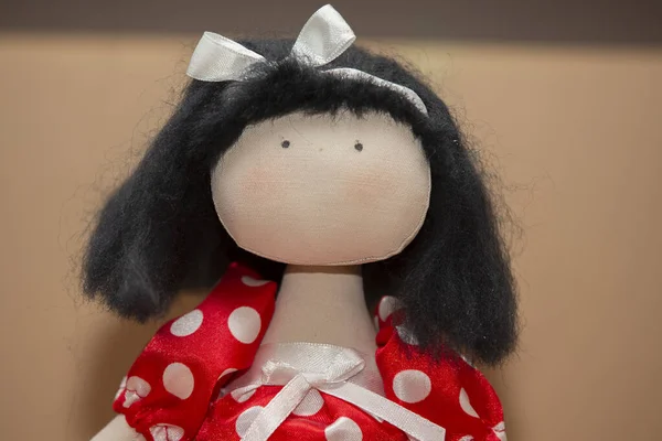 Doll made of handmade fabrics. Portrait of a doll in a red dress with polka dots, only eyes are painted on her face.