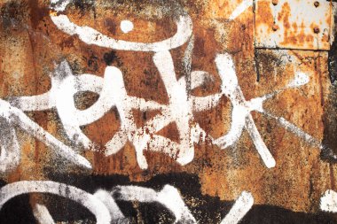 Paslı bir demir duvarda soyut beyaz boya çizimleri var..