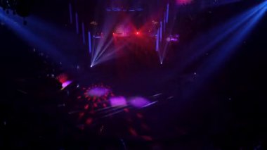 Sirk arenası seyircilerinin parlak sahne ışıkları önünde aydınlatılmış siluetleri. Karanlık arka plan, konser ışıkları