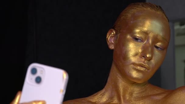 这个模特的脸涂上了金色的油漆 看着一部手机 — 图库视频影像