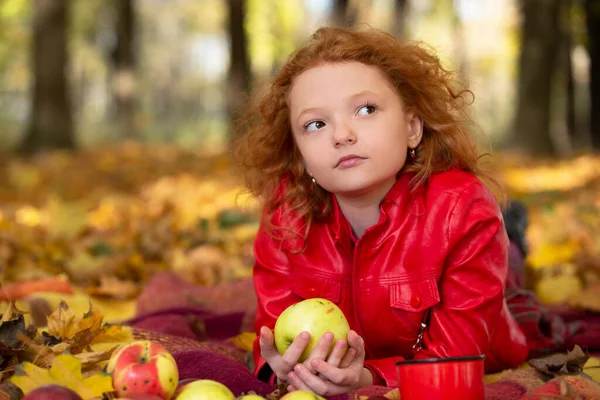 Sad red-haired girl with an apple in the autumn park.