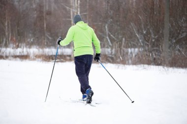 Parlak elbiseli bir adam kış ormanında kayak yapıyor..