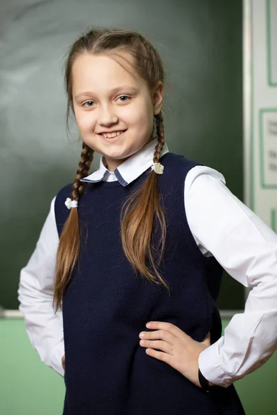 Funny schoolgirl with pigtails, middle school age on the background of the blackboard.