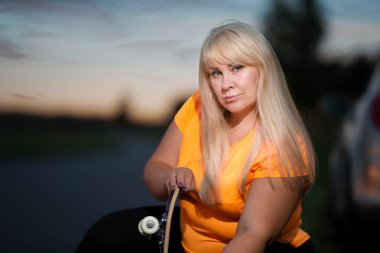 Portrait of a plump european woman in a sports tank top with a skateboard.