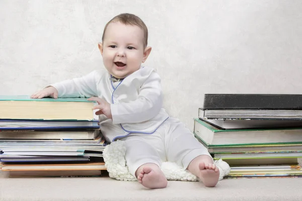 Little child among books. Happy six month old baby boy in a stack of books. The concept of early childhood education.