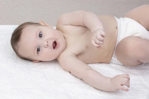 A six-month-old baby boy in a diaper lies on a diaper. The concept of motherhood and fatherhood.