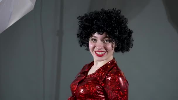 在演播室里 一个身穿黑色假发和红色连衣裙的漂亮女孩在镜头前摆姿势 — 图库视频影像