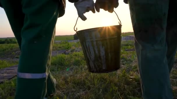 Två Arbetare Bär Hink Olja Vid Solnedgången — Stockvideo